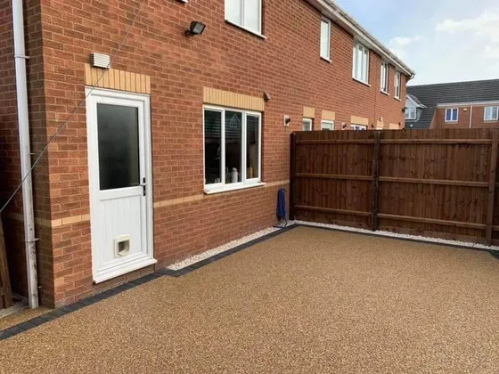 Artificial lawn set into a golden resin bound patio with a charcoal block edge