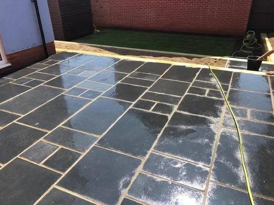 Wet black limestone patio slabs laid in a random pattern