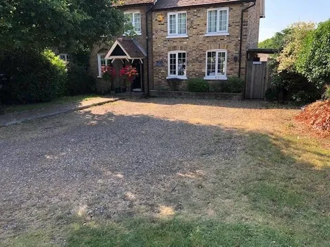 Bare earth and loose gravel in front of a brick cottage before the block paving