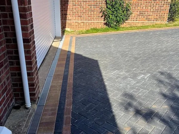 Charcoal herringbone block paving with a buff border and a drainage channel along a garage wall