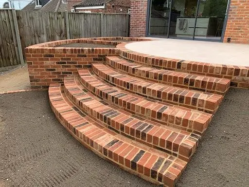 Curved red-brick steps and retaining wall leading up to a raised patio