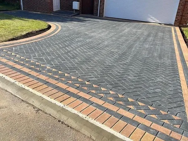 Charcoal herringbone block paving with a buff double border curving round a front lawn