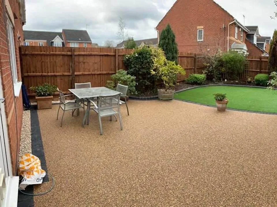 Back garden with a golden resin bound patio, table and chairs, artificial lawn and planted borders, landscaped by First4Driveways