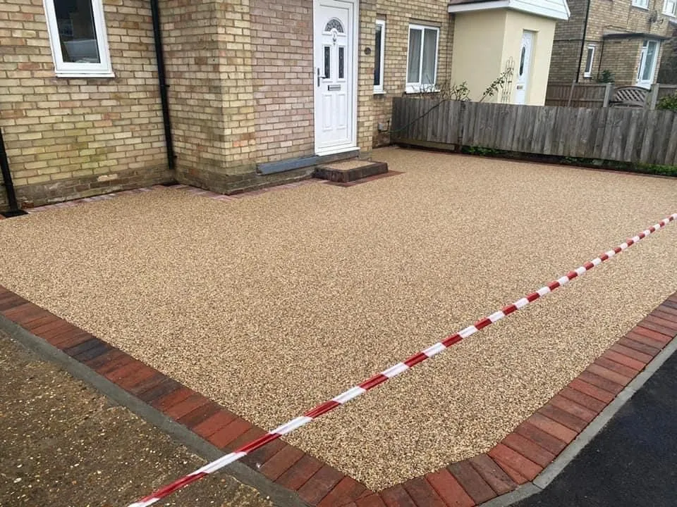 Golden resin bound driveway with a red brick border in front of a brick semi, laid by First4Driveways