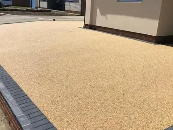 Golden resin bound driveway with a charcoal block paving edge beside a bungalow