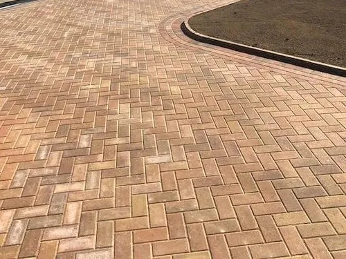 Buff herringbone block paving driveway curving round a lawn with a contrasting border
