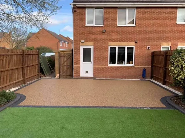 Back garden with a golden resin bound patio and an artificial lawn behind a brick house