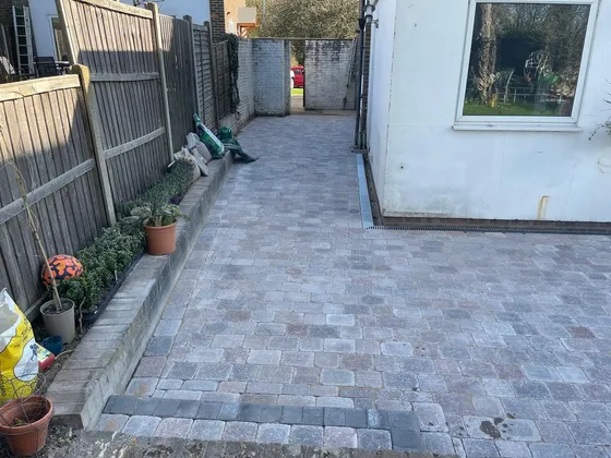 Grey tumbled block paving patio and path running along the side of a white rendered house