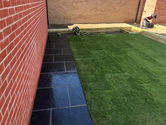 New turf laid beside a black limestone path against a red-brick wall