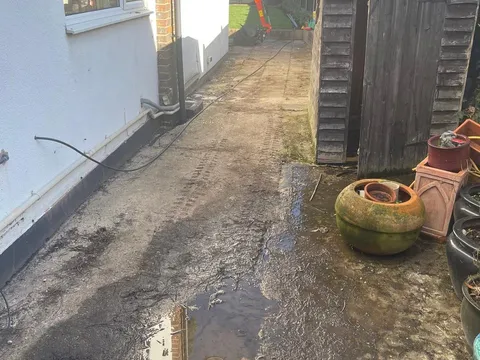 Muddy ground and old slabs along the side of a white rendered house before the work