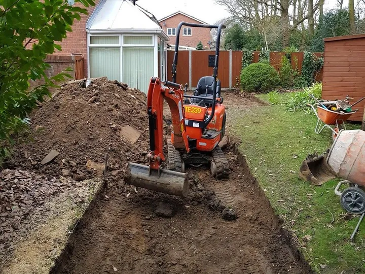 Small digger excavating the ground beside a lawn to make room for a new patio base
