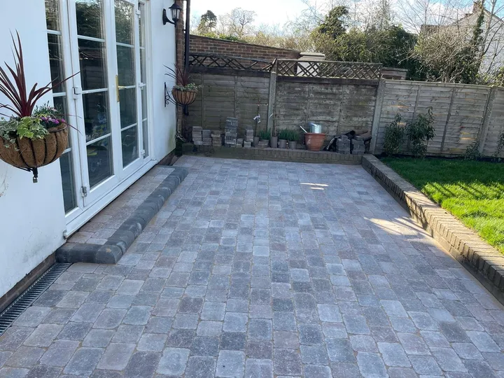 Grey tumbled block paving patio outside French doors with a raised edge to the lawn, laid by First4Driveways