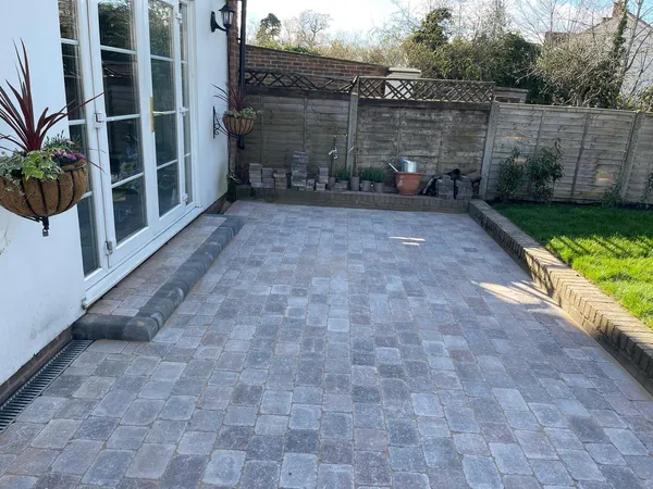 Grey tumbled block paving patio outside French doors with a raised edge to the lawn
