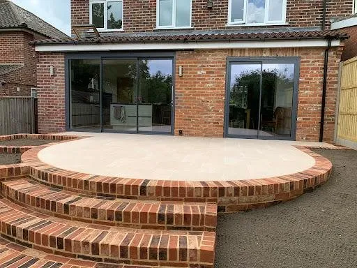 Raised buff porcelain patio on a curved red-brick retaining wall