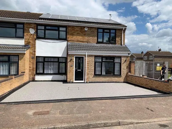 Silver resin bound driveway with a black resin border in front of a buff-brick semi