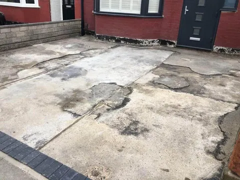 Patched and cracked concrete in front of a red-brick house before the work