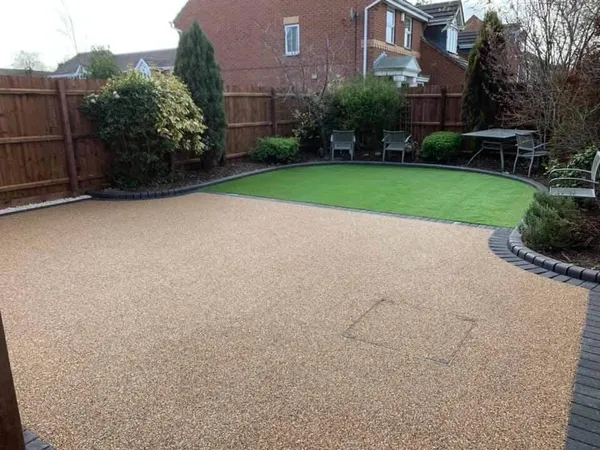 Golden resin bound patio with charcoal block edging beside a circle of artificial grass
