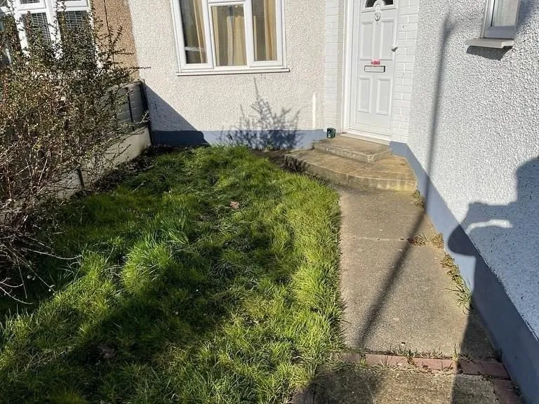 White bungalow with a lawn and narrow concrete path before the new driveway