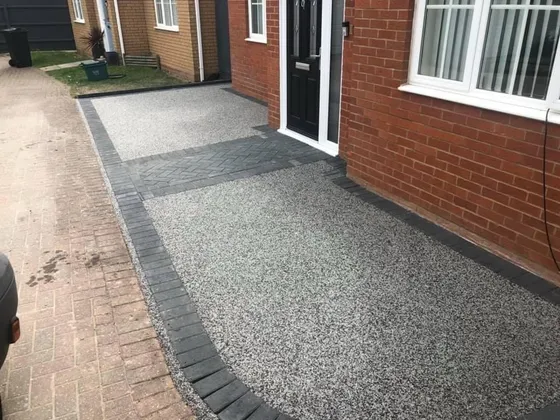 Silver resin bound driveway with a charcoal block paving border along the house