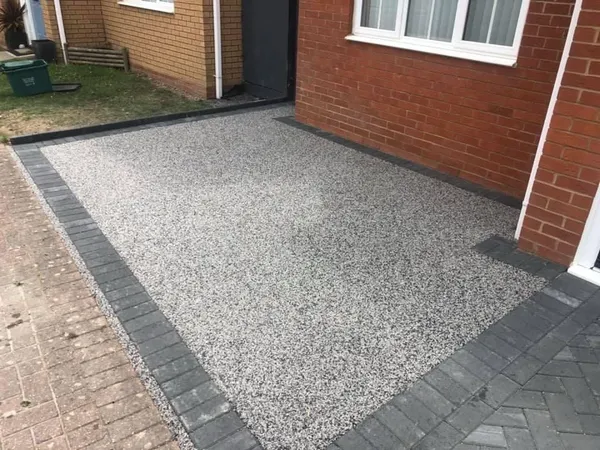 Silver-grey resin bound driveway with a charcoal block paving border beside a red-brick house
