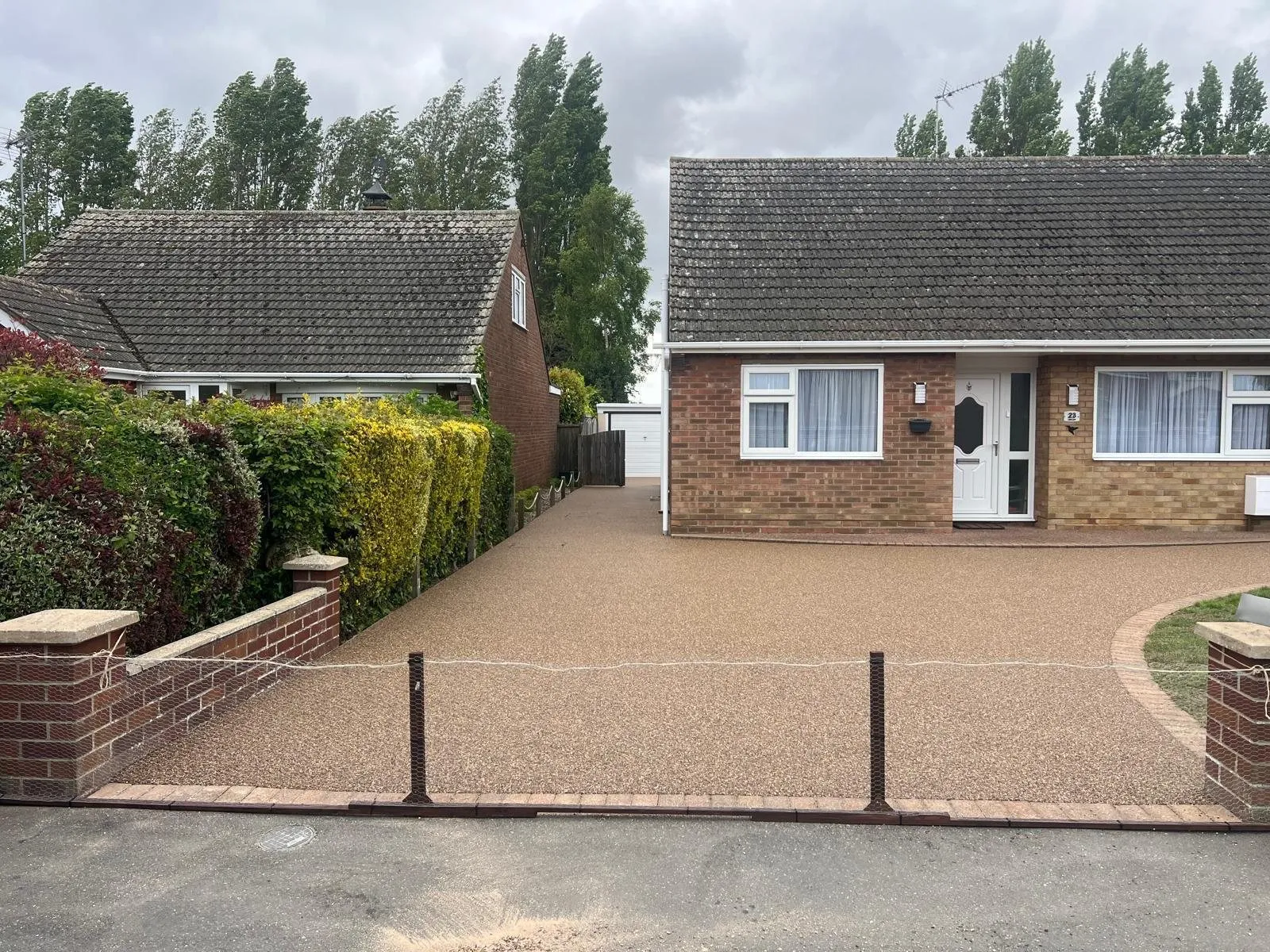 Golden resin bound driveway in front of a brick bungalow with a lawn and low wall, laid by First4Driveways
