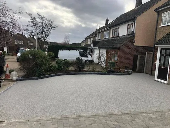 Silver-grey resin bound driveway curving round a planted bed in front of a semi
