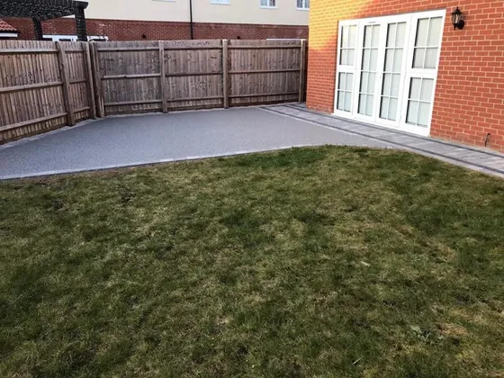 Silver resin bound patio at the back of a red-brick house with a lawn in front