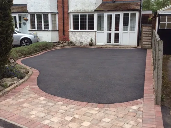 Black tarmac driveway with a curved brindle block border in front of a mock-Tudor semi