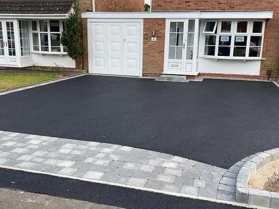 Black tarmac driveway with a grey block border and a gravel margin in front of a brick house