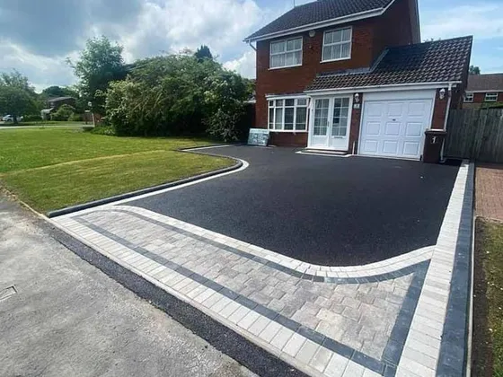 Black tarmac driveway with a light block border running up to a red-brick detached house