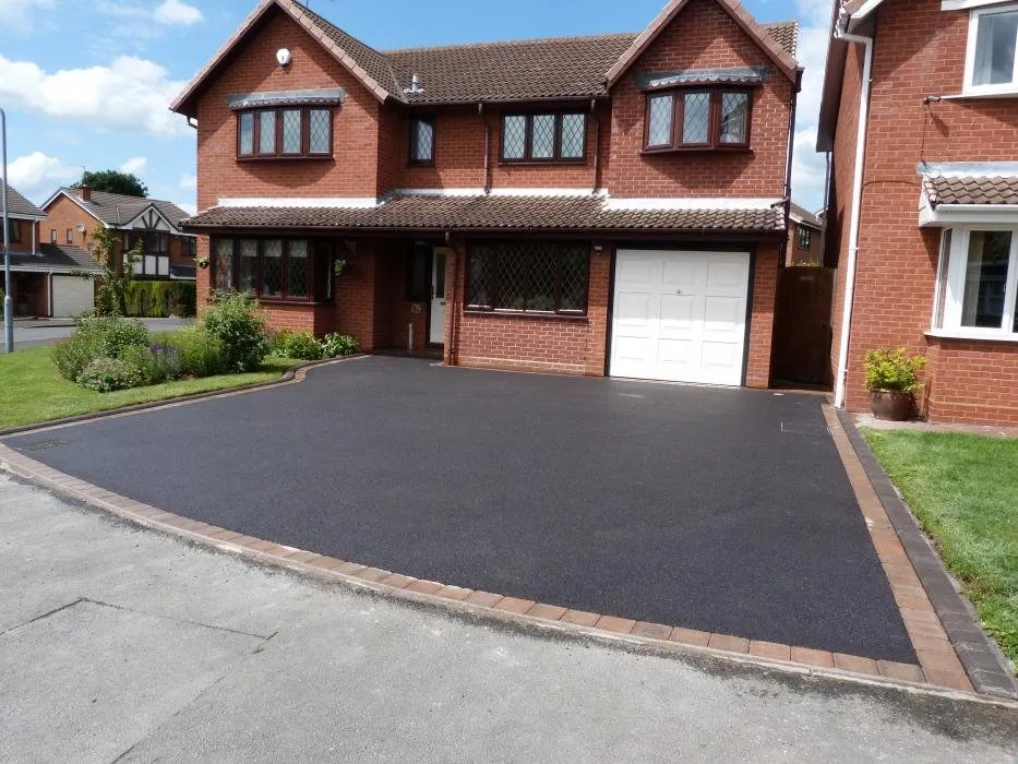 Black tarmac driveway with a red block border at a red-brick detached house, laid by First4Driveways