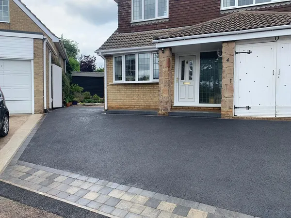 Black tarmac driveway with a grey block paving border in front of white garage doors