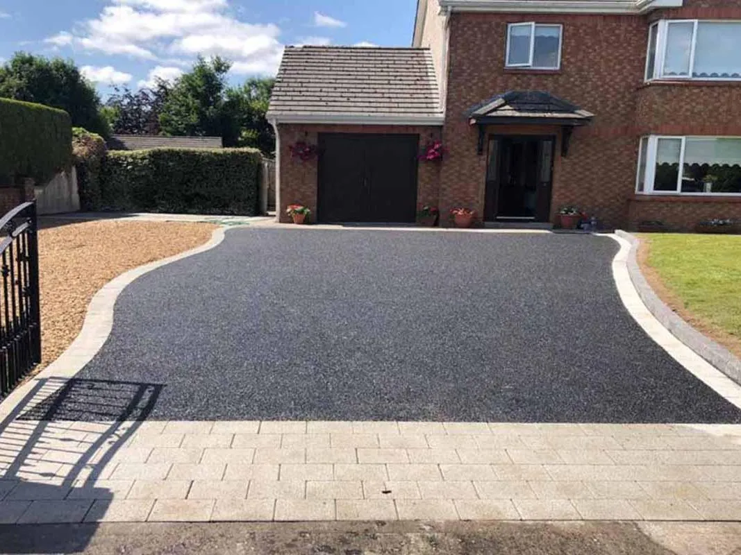 Sweeping black tarmac driveway with grey block edging and a gravel margin in front of a white house with an iron gate