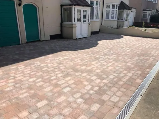Pink and brindle tumbled block paving with a drainage channel along the front of a garage