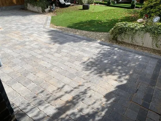 Grey tumbled block paving patio beside an artificial lawn and a bed of shrubs